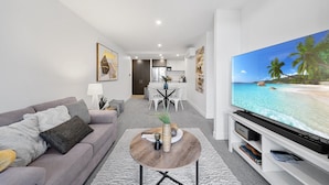 Ein modernes Wohnzimmer mit grauem Sofa, rundem Couchtisch und einem Flachbildfernseher, der eine Strandansicht zeigt.