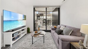 Ein modernes Wohnzimmer mit Flachbildfernseher, einer Couch, einem Couchtisch und Blick auf einen Balkon.