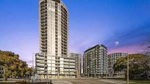 Ein modernes Hochhaus mit geschwungener Fassade, mehreren Balkonen und einem Fußweg davor.