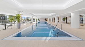 Ein modernes Hallenbad mit klarem, blauem Wasser, umgeben von Liegebereichen und großen Fenstern.