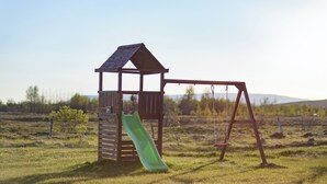 A wooden play structure with a slide and swings in a grassy field.