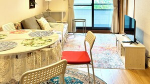 Een gezellige woonkamer met een bank, een eettafel met placemats, een televisie en een groot raam met gordijnen.