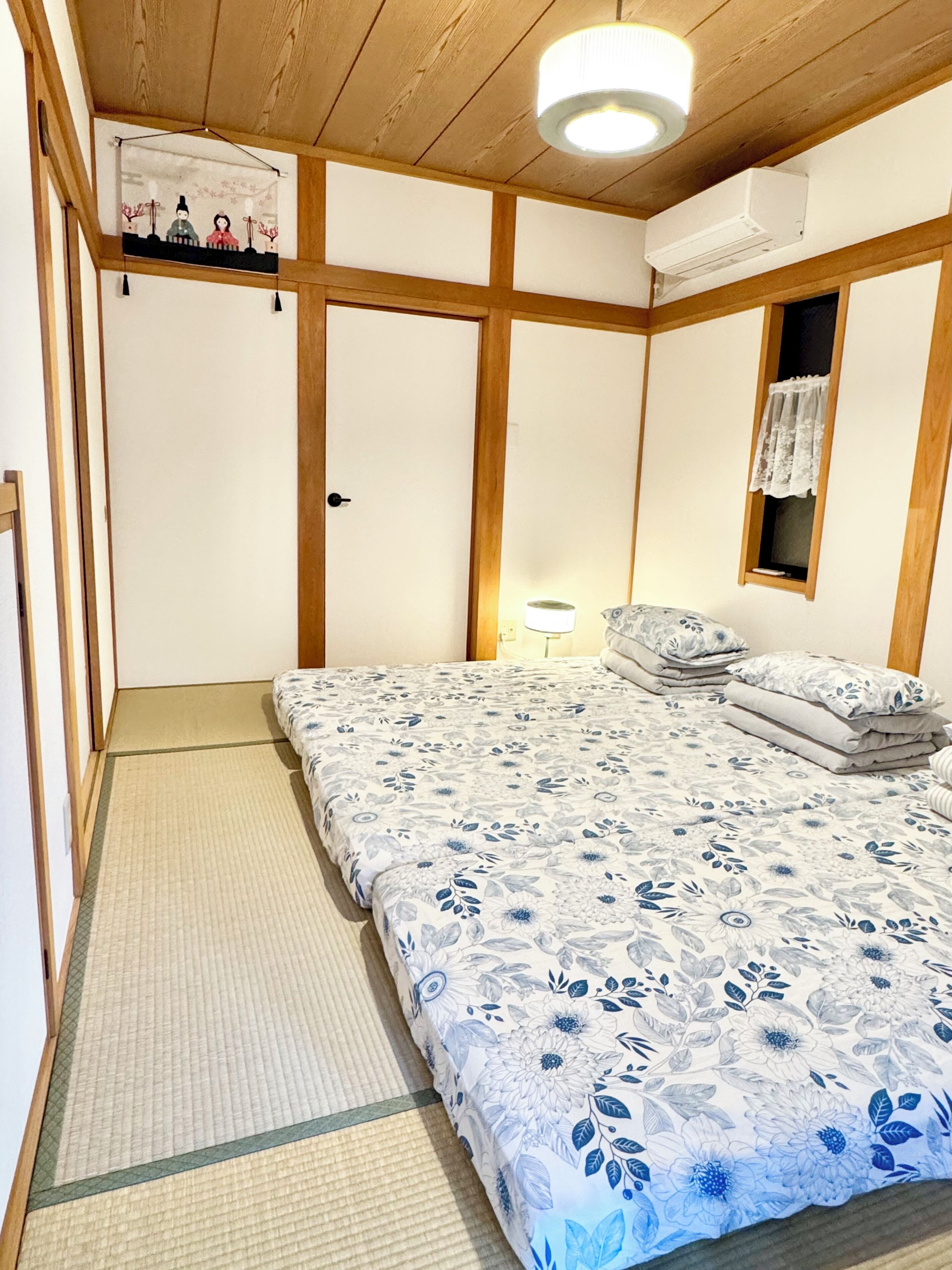 Una camera da letto tradizionale in stile giapponese, con pavimento in tatami, un letto con copriletto floreale, una porta scorrevole shoji e una ventola a soffitto.