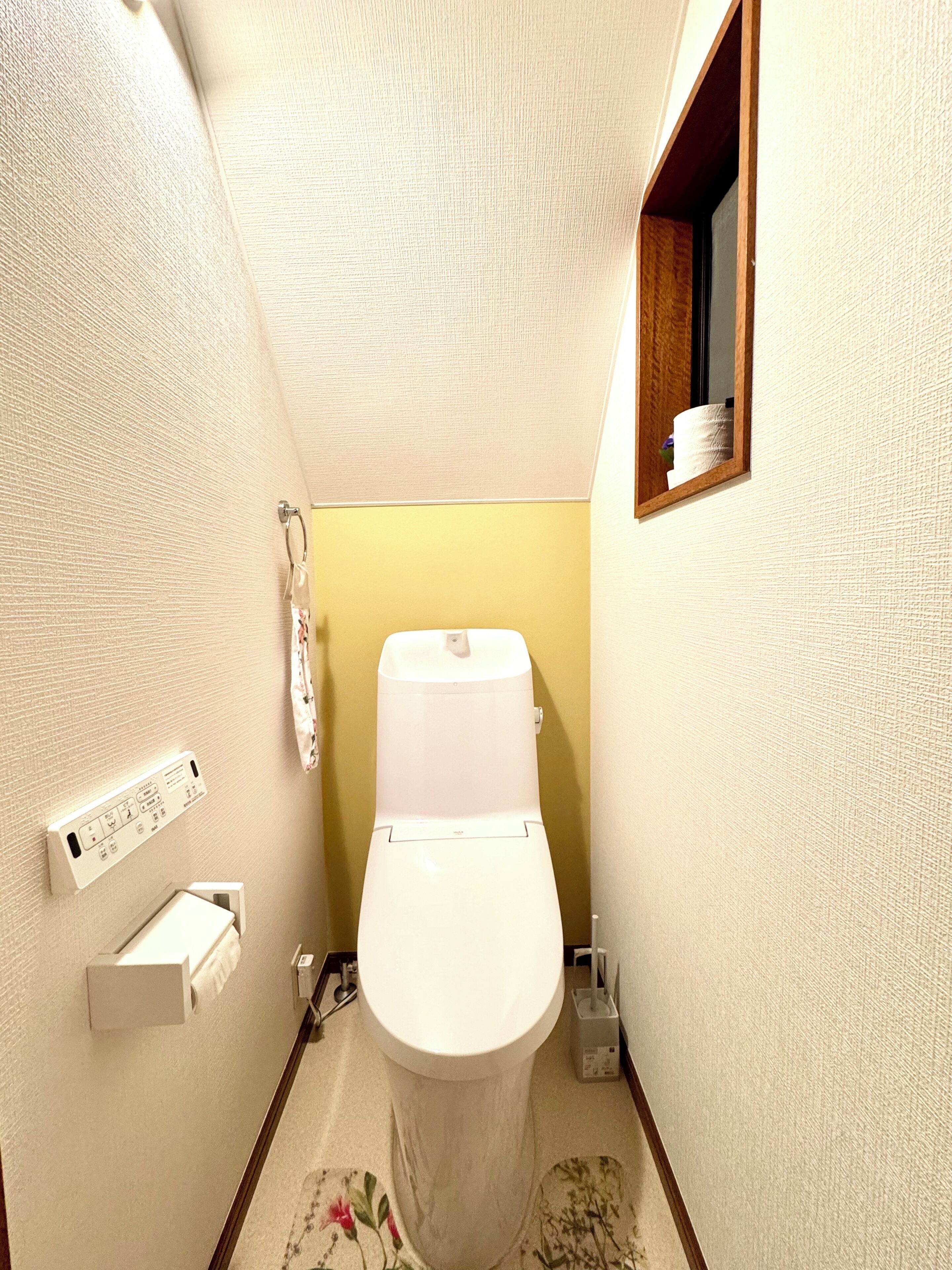 A small, narrow bathroom with a toilet, a hand dryer, and a small shelf with toiletries.