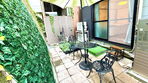Een terras met een tafel, stoelen, een grote parasol en uitzicht op een gebouw met een raam.