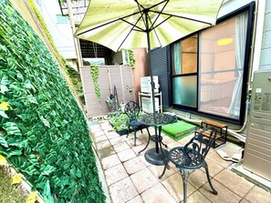 Een terras met een tafel, stoelen, een grote parasol en uitzicht op een gebouw met een raam.