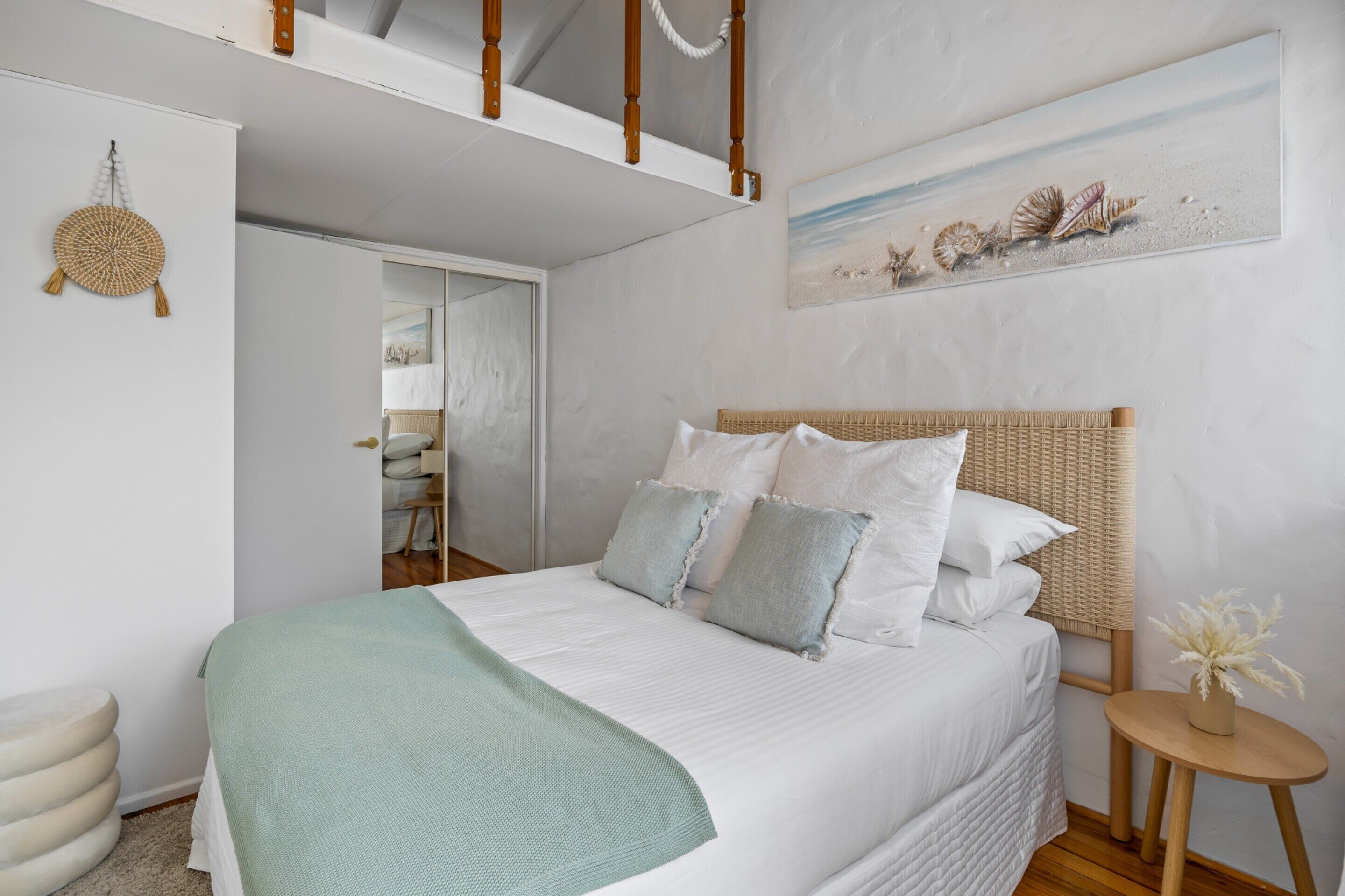 A bedroom with a bed, a woven headboard, a round wall hanging, and a painting of shells.
