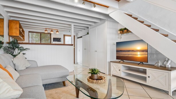 A modern living room with a glass coffee table, a grey sofa, and a TV on a wooden stand. - Chic 2-bed Cabin-style Home by Mooloolaba Beach (Sunshine Coast)