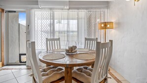 A dining area with a round table, cushioned chairs, a glass vase with stones, and a wall-mounted lamp. - Chic 2-bed Cabin-style Home by Mooloolaba Beach (Sunshine Coast)