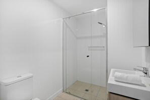 Un baño moderno con cabina de ducha de vidrio, lavamanos blanco y un inodoro.