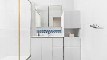 A modern bathroom with white cabinetry, a blue-tiled backsplash, and a glass shower enclosure.