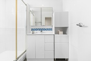 Un baño moderno con muebles blancos, salpicadero de azulejos azules y cabina de ducha de vidrio.