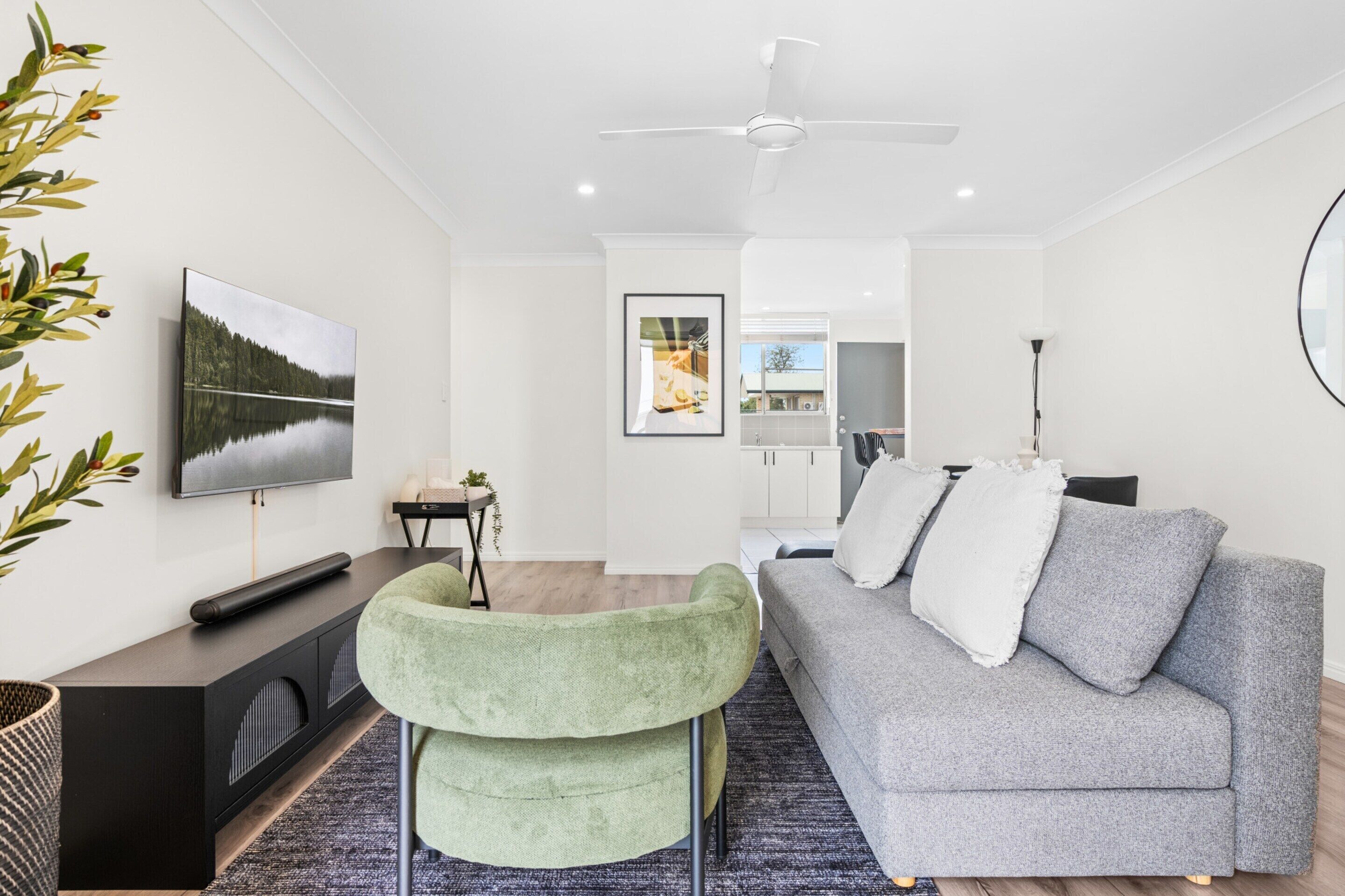 A modern living room with a grey sofa, a green armchair, a flat-screen TV, and a ceiling fan.