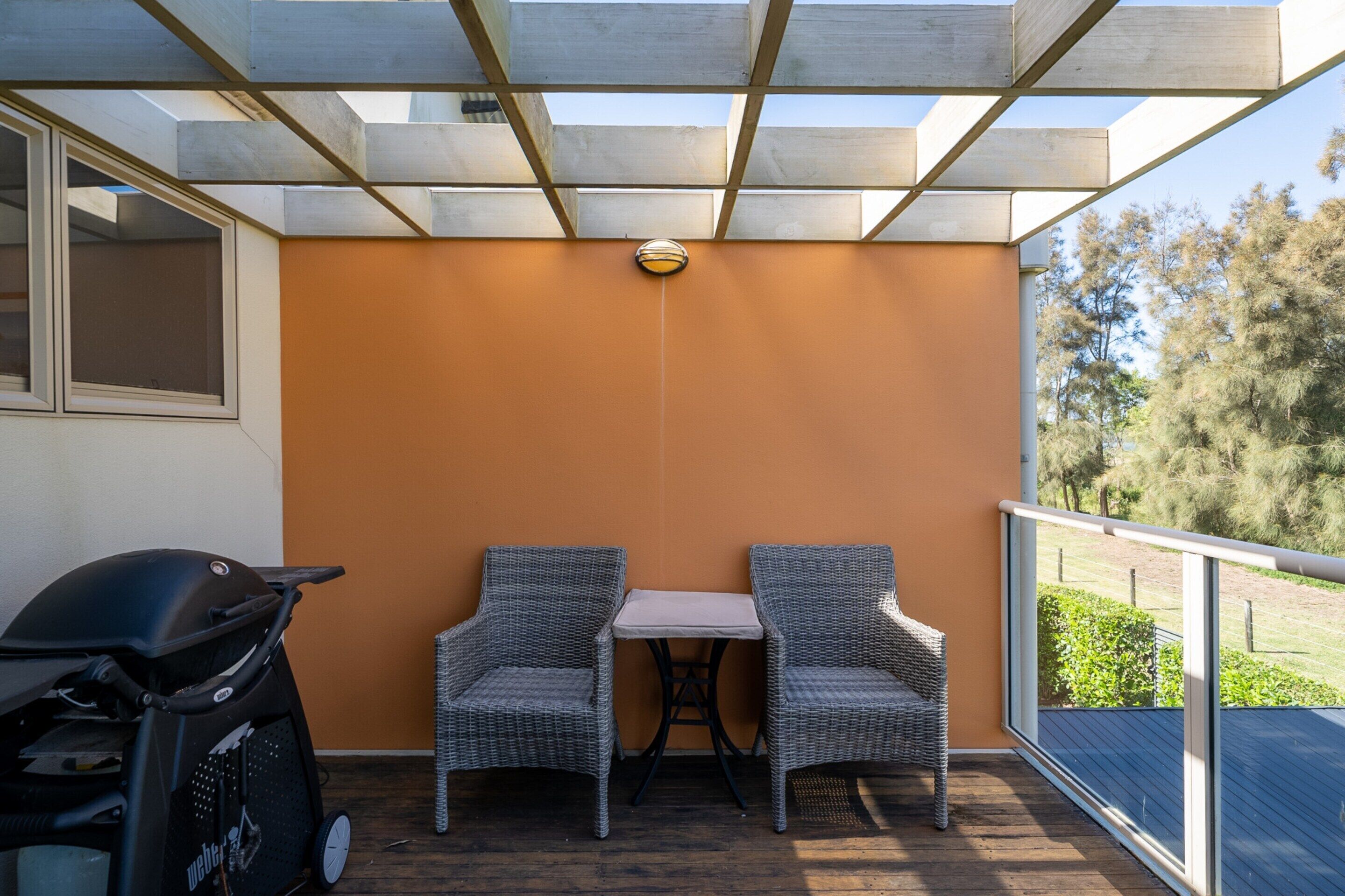 A balcony with two wicker chairs, a small table, and a grill.