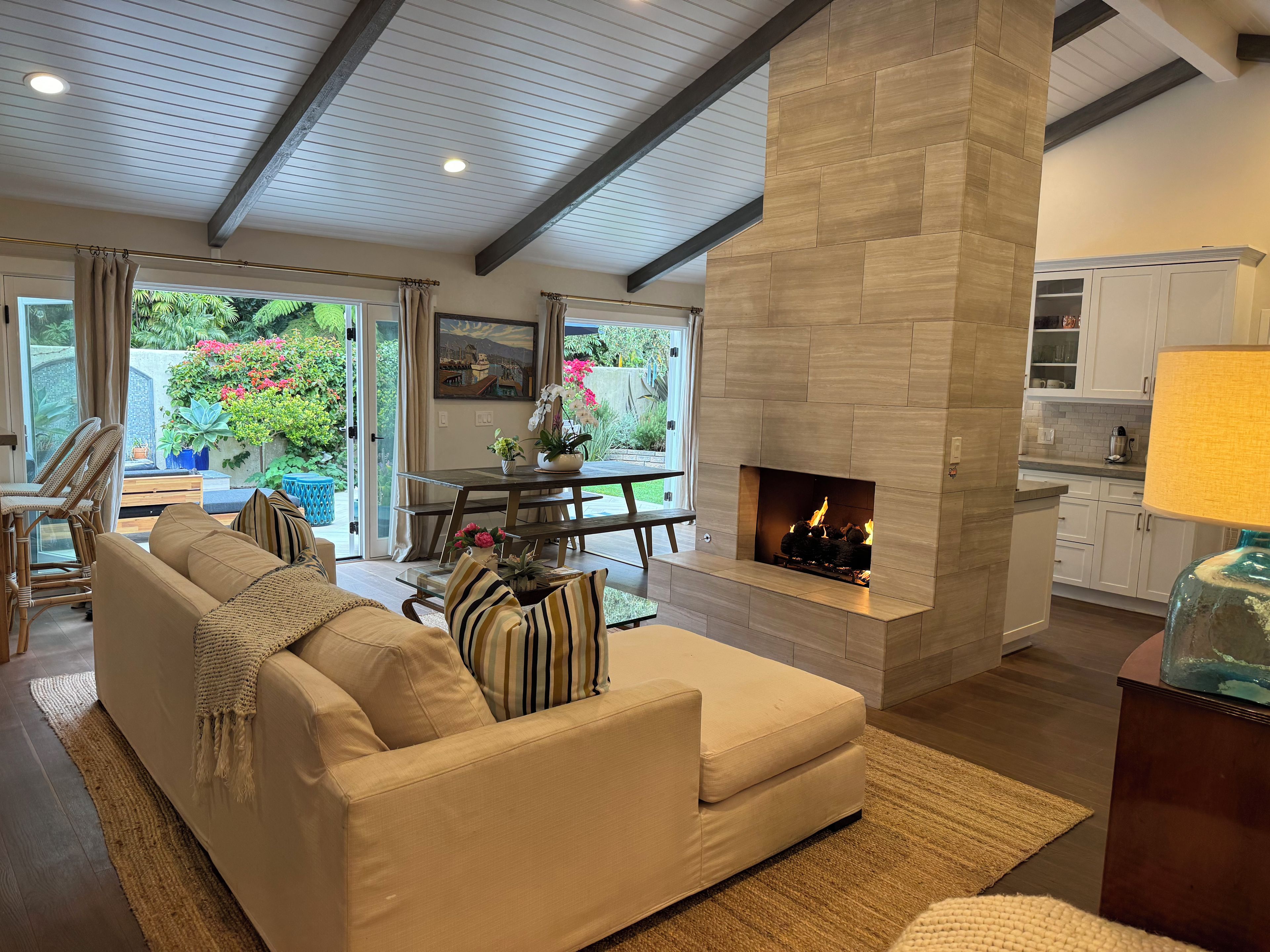 A living room with a fireplace, a sofa, a dining table, and a view of the outdoors.