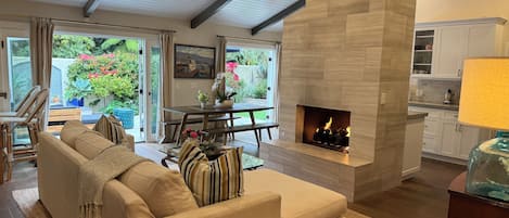 A living room with a fireplace, a sofa, a dining table, and a view of the outdoors.