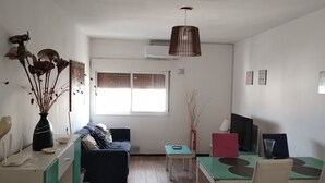 A modern living room with a sofa, a dining table with chairs, a coffee table, a TV, and a decorative vase with dried plants. - BOULEVARD APARTMENT (Rosario)