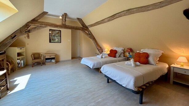 Une chambre avec deux lits, des poutres en bois, un tableau et une petite table avec une lampe.