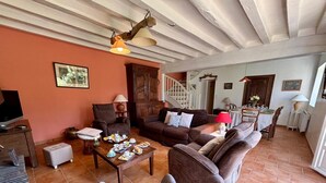 A cozy living room with a sofa set, a coffee table with snacks, a TV, and a staircase leading to another room.