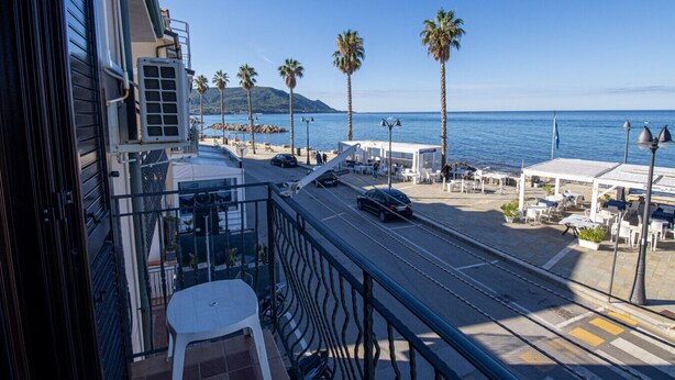 Un balcon avec vue sur la mer, des palmiers et une rue animée.