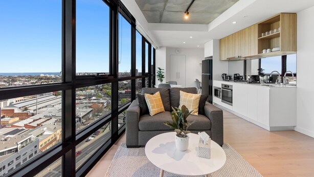 A modern apartment with a large window, a kitchen, and a living area with a sofa and a coffee table. - Stylish 1-bed With Pool Gym & Stunning Views (Melbourne)