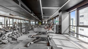 A modern gym with various exercise equipment, large windows, and a high ceiling. - Stylish 1-bed With Pool Gym & Stunning Views (Melbourne)
