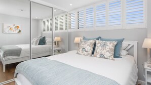 Un dormitorio moderno con una cama grande, un espejo y una ventana con contraventanas.