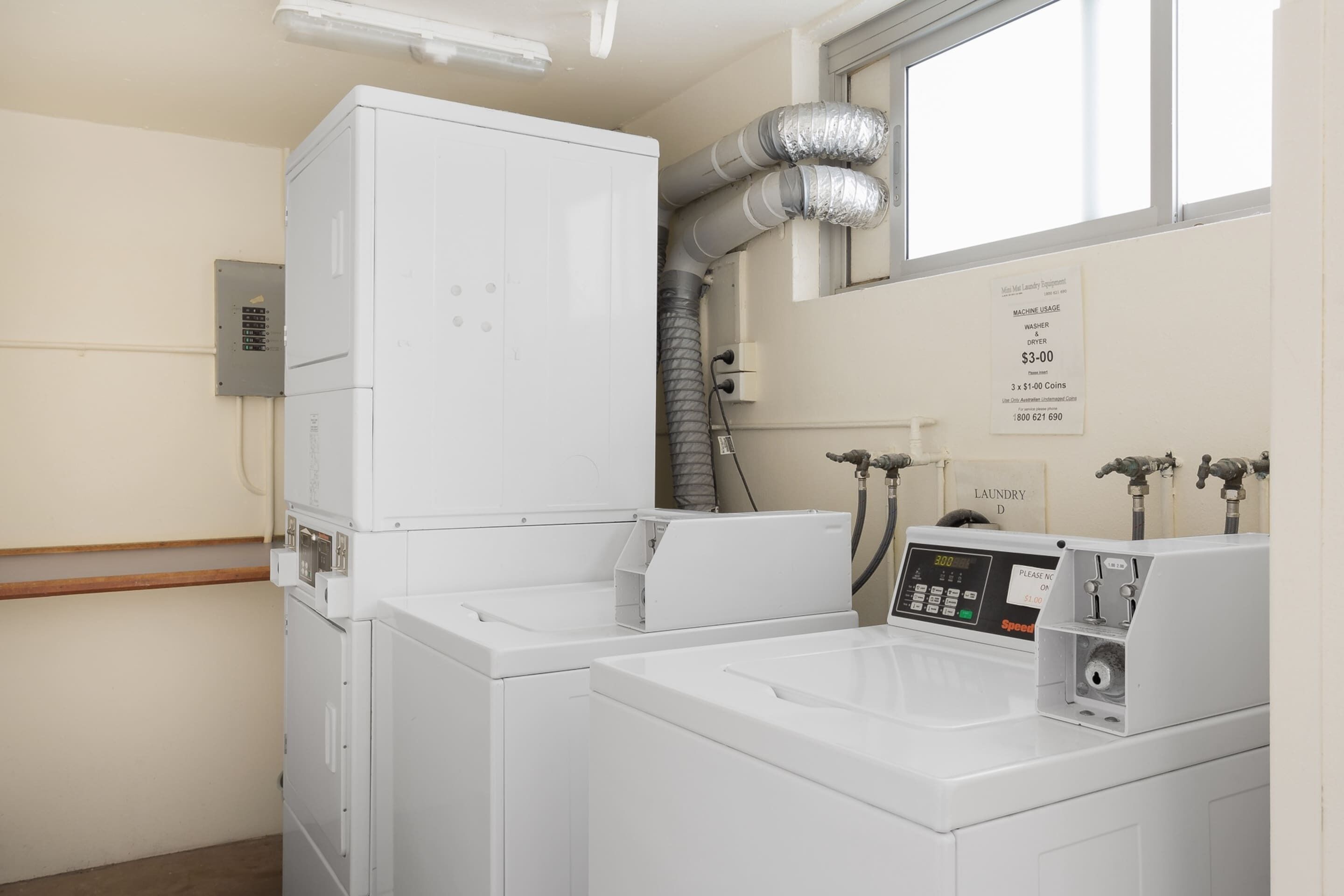 A laundry facility with stacked washing machines, a dryer, and a control panel.