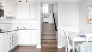 Una cocina moderna con armarios blancos, una escalera de madera y un comedor con sillas y mesa blancos.