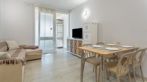 Een moderne woonkamer met een bank, een eettafel met stoelen, een televisie en een kast.