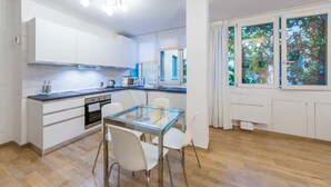 A modern kitchen with white cabinets, a glass dining table, and a view of trees through the window. - HouSmart Val D'Aposa 5  (Bologna)