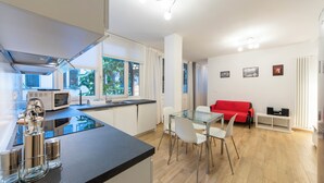 A modern kitchen with a glass dining table, white chairs, and a red sofa in the living area. - HouSmart Val D'Aposa 5  (Bologna)