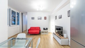 A modern living room with a glass table, a red sofa, a TV, and a refrigerator. - HouSmart Val D'Aposa 5  (Bologna)