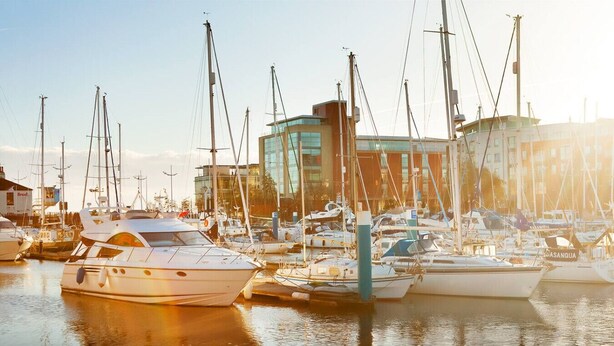 A marina with multiple boats docked, a modern building in the background, and calm water reflecting the boats. - 2 Bedroom Marina Suite-203 (Kingston upon Hull)