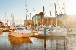 A marina with multiple boats docked, a modern building in the background, and calm water reflecting the boats.