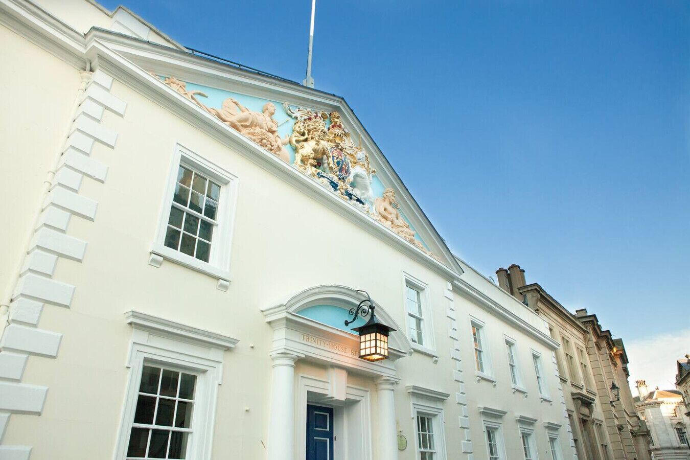 A building with classical architecture, featuring a prominent balcony with decorative sculptures and a blue sky in the background.