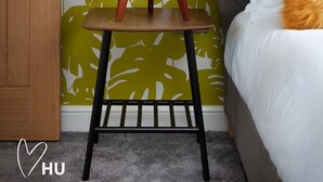 A room with a wooden door, a green patterned wall, a small wooden table with a white lamp, a grey sofa, and a white pillow with an orange accent. - 2 Bedroom Marina Suite-203 (Kingston upon Hull)