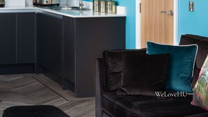 A modern kitchen with dark cabinets, a teal accent wall, and a wooden door. - We Love HU -Sky Marina Suite (Kingston upon Hull)