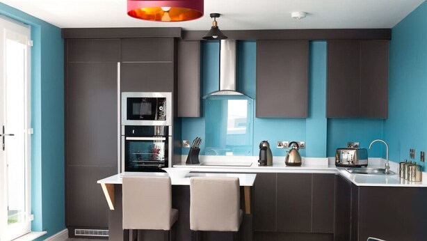 A modern kitchen with dark cabinets, a central island with bar stools, and a window providing natural light. - We Love HU -Sky Marina Suite (Kingston upon Hull)