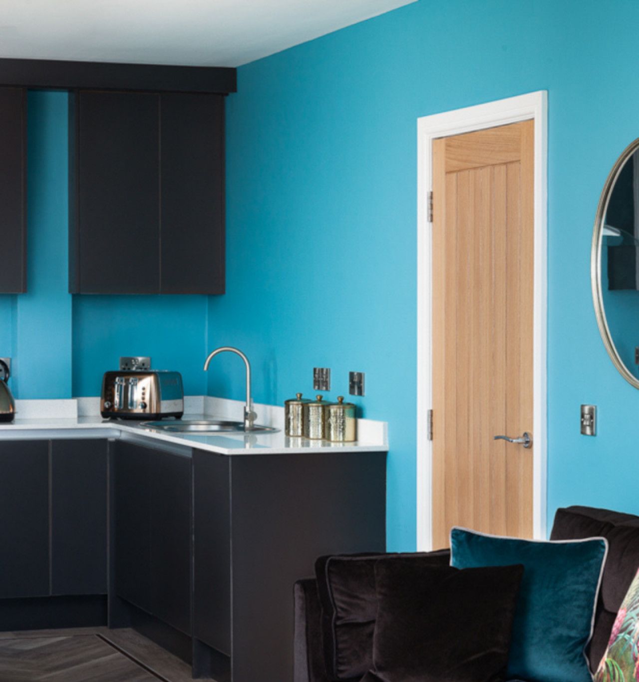 Una cocina moderna con armarios oscuros, una pared de acento color aguamarina y una puerta de madera.