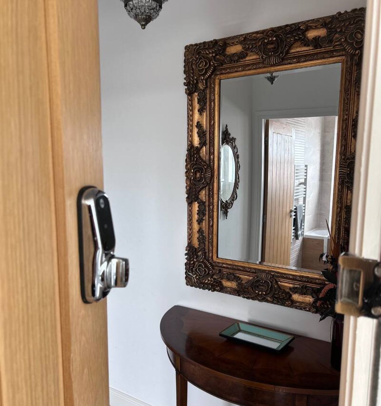 A wooden door with a modern handle, a mirror with an ornate frame, and a small table with a green object on it.
