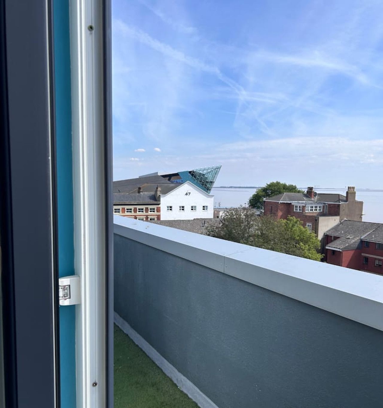 Uitzicht vanaf een balkon, heldere lucht, een gebouw met nummer 47 en een waterpartij op de achtergrond.