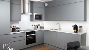 Una cocina moderna con gabinetes grises, una campana extractora de acero inoxidable, un microondas, un fregadero y un hervidor.
