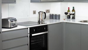 Una cocina moderna con armarios grises, microondas integrado, tostadora, horno y hervidor. Hay botellas de vino y copas sobre la encimera.