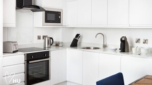 Una cocina moderna con armarios blancos, horno integrado, microondas, hervidor, cafetera y lavabo.