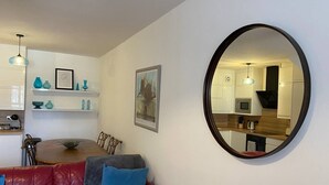 Sala de estar con un sofá de cuero rojo, una mesa de comedor y una cocina visible en un espejo.