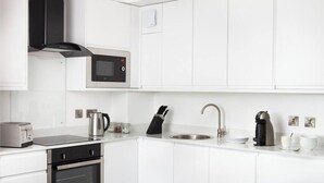 Una cocina moderna con armarios blancos, horno integrado, microondas, hervidor, cafetera y lavabo.