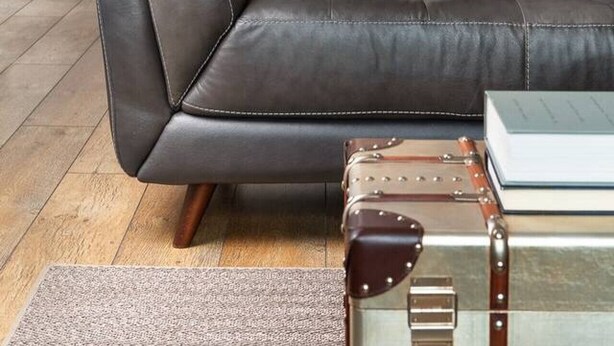 Una sala moderna con un sofá de cuero, un cojín a rayas y una maleta antigua.