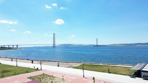 A view of a bridge over water with a pedestrian path and grass in the foreground. - Orçın Apartmanı (Lapseki)