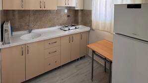 A modern kitchen with beige cabinets, a white countertop, a sink, a gas stove, and a refrigerator. - Orçın Apartmanı (Lapseki)